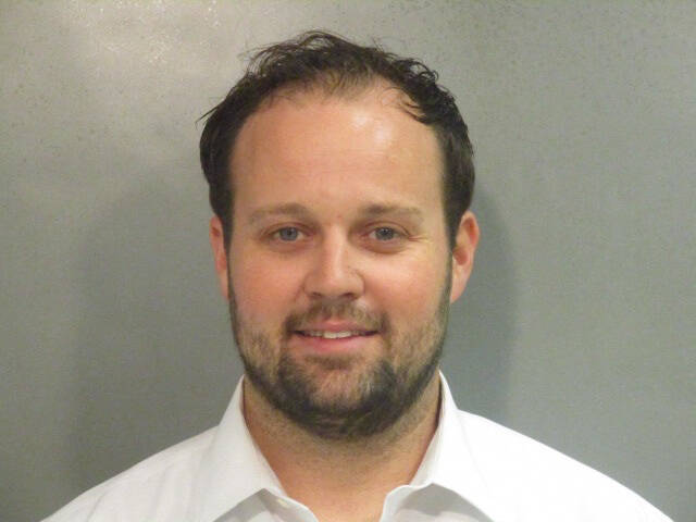 Josh Duggar in a mugshot photo wearing a white collared shirt, looking at the camera with a slight smile.